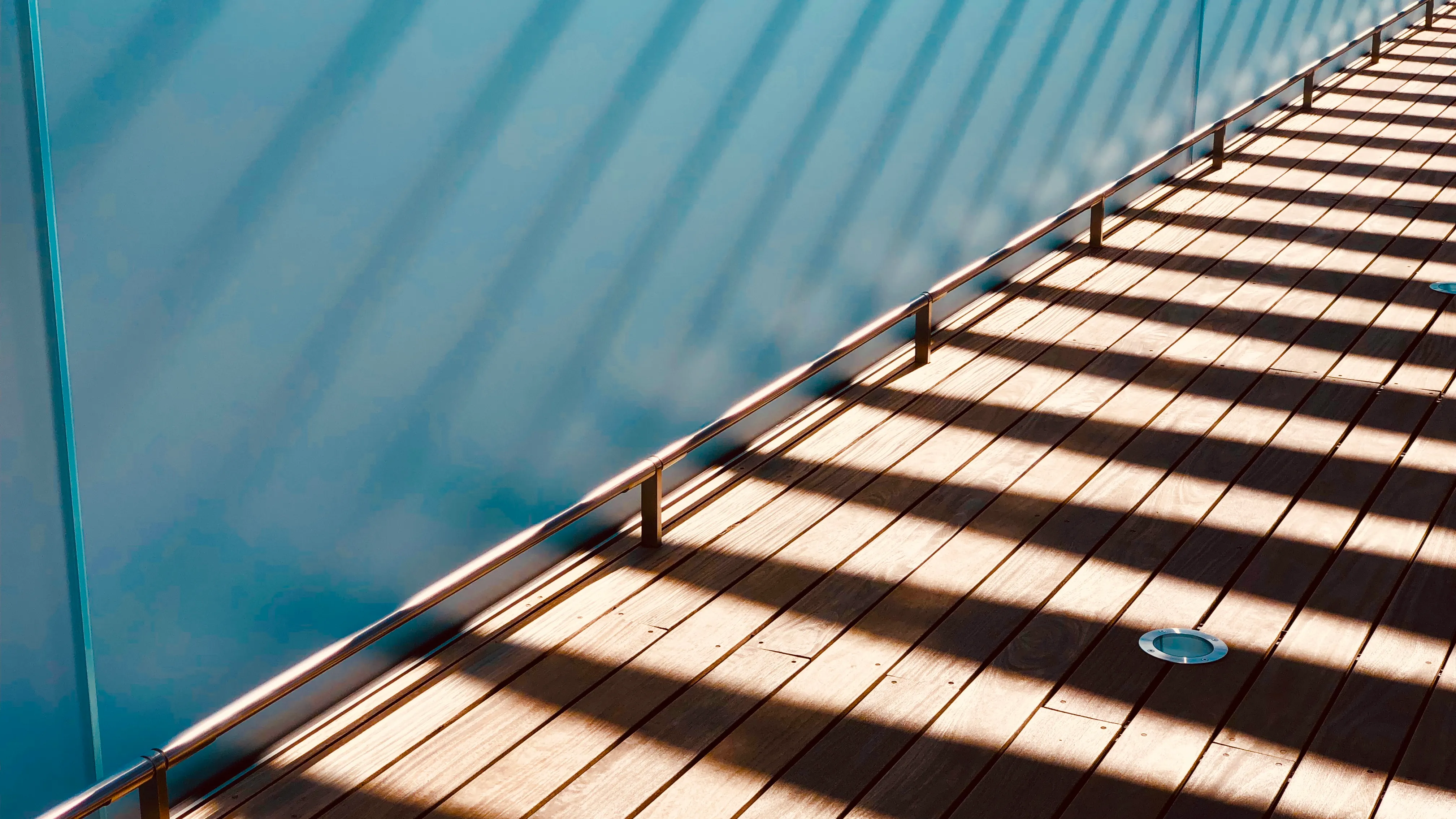 Shadows and light on outdoor floorboards, against a glass wall